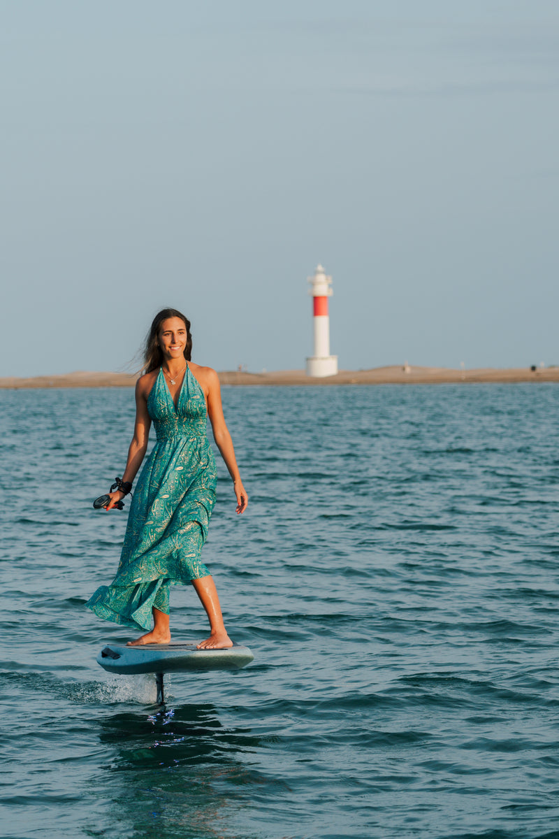 Mujer con vestido verde sobre el Flyer EVO junto a un faro al atardecer