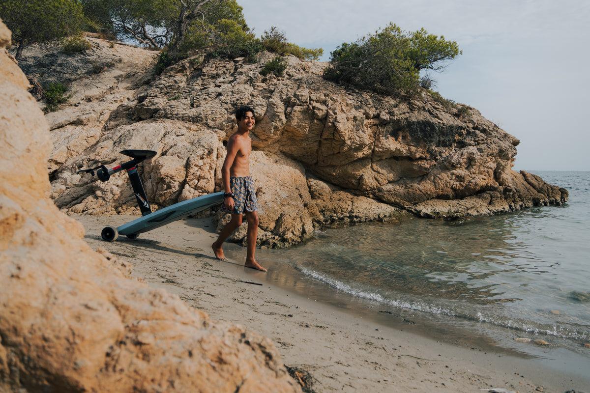 Hombre cargando una tabla Flyer EVO por una playa rocosa