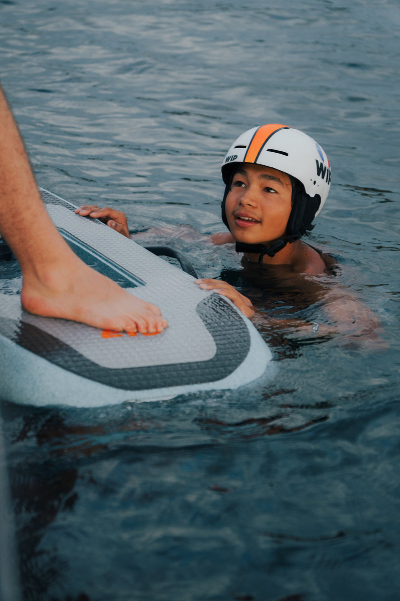 Adolescente tumbado sobre la tabla del Flyer EVO sonriendo, con casco puesto